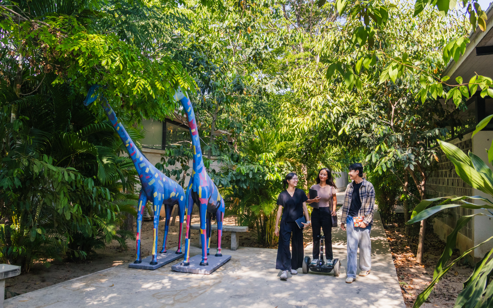 Three coworkers walking along a shaded garden pathway at Aquation Office Park next to two colorful giraffe statues.
