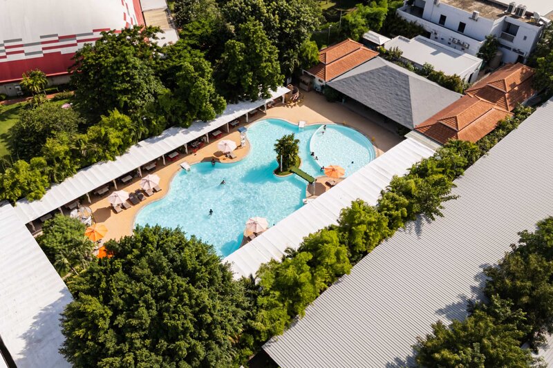 High aerial view showing the pool area, surrounding roofs, and green trees.
