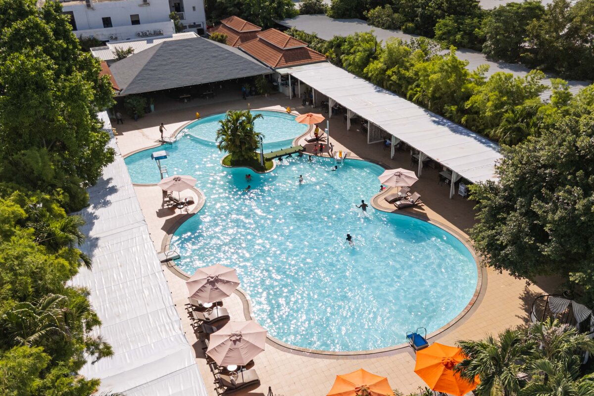 High angle view of the sunny outdoor swimming pool with loungers and umbrellas at DIB Club, Phnom Penh.