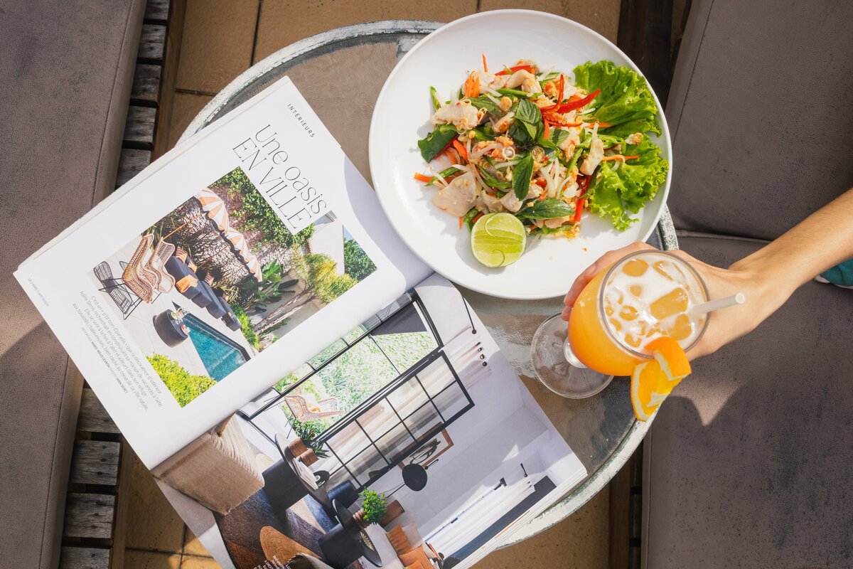 Fresh chicken salad plate, open magazine, and iced drink on a table at DIB Club, Phnom Penh.