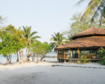 Exterior view of the Beach Bar surrounded by palm trees and white sand on the shore at Island Center Point hotel, Koh Rong Sanloem.