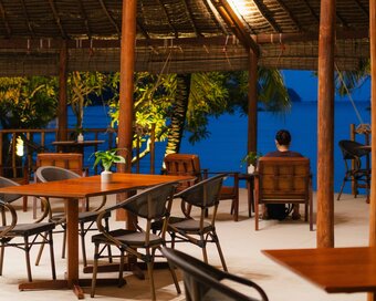 Wooden tables and chairs set inside the open-air beach bar overlooking the sea during evening at Island Center Point hotel, Koh Rong Sanloem.