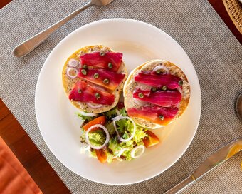 Top-down view of a plate with two open-face gravlax bagels, bread basket, and drinks at Island Center Point hotel, Koh Rong Sanloem.