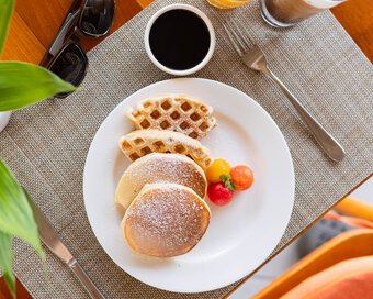 Overhead shot of pancakes and waffles, served with fruit, fresh passion juice, and iced coffee at Island Center Point hotel, Koh Rong Sanloem.