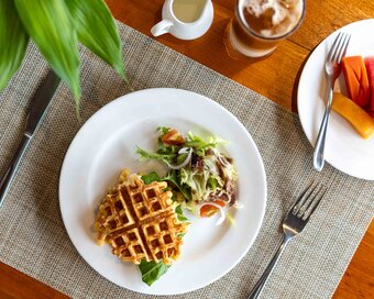 Top-down view of waffle with eggs served with a side salad, fresh fruit, and iced coffee at Island Center Point hotel, Koh Rong Sanloem.