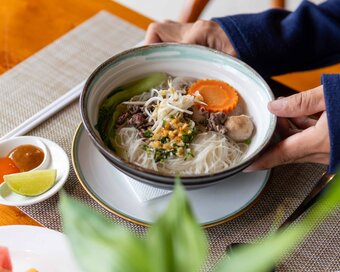 Guest holding a warm bowl of rice noodle soup with beef, vegetables, Island Center Point hotel, Koh Rong Sanloem.