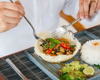 Guest using a fork and spoon to eat stir-fried dish alongside steamed rice at Island Center Point hotel, Koh Rong Sanloem.