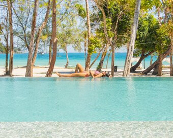 An islander lounging poolside in a swimsuit under sunny skies, turquoise water at the background, and white sandy shore at Island Center Point, Koh Rong Sanloem.