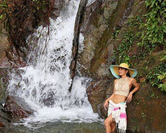 Woman wearing sun hat posing beside a cascading natural waterfall, rocky jungle setting in Saracen Bay, Koh Rong Sanloem.