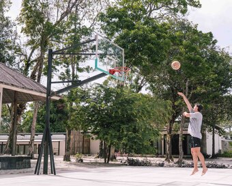 Islander going up for a jump shot on an outdoor basketball court surrounded by tall trees at Island Center Point hotel, Koh Rong Sanloem.