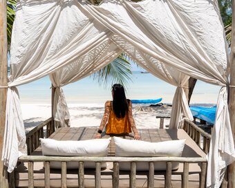 Island seeker relaxing inside a shaded wooden beach cabana looking out toward the ocean in Koh Rong Sanloem.