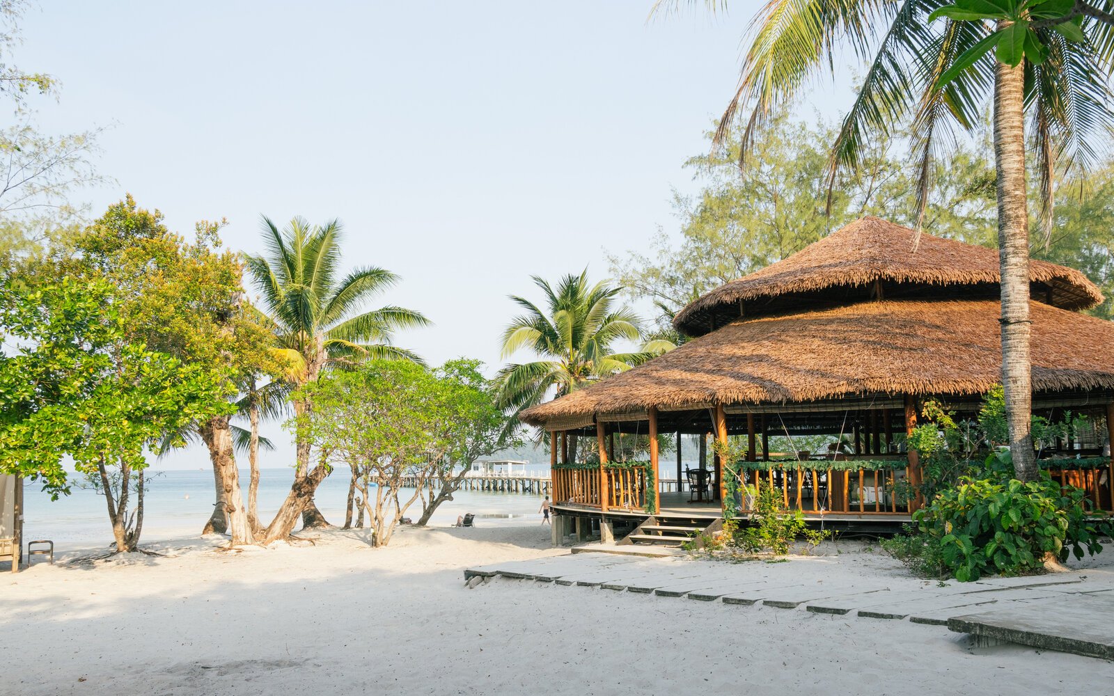 Daytime view of the round wooden beach bar nestled among palm trees on a clean white sand beach at Island Center Point, Koh Rong Sanloem.