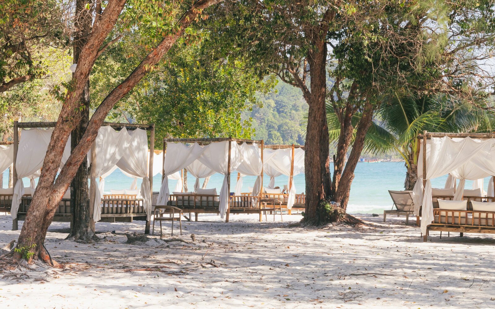 Row of shaded beach cabanas with white curtains set under trees along the sand of Saracen Bay, Koh Rong Sanloem