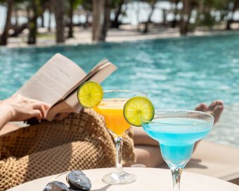 Two colorful tropical cocktails by the pool with a guest reading in the background, at Island Center Point, Koh Rong Sanloem
