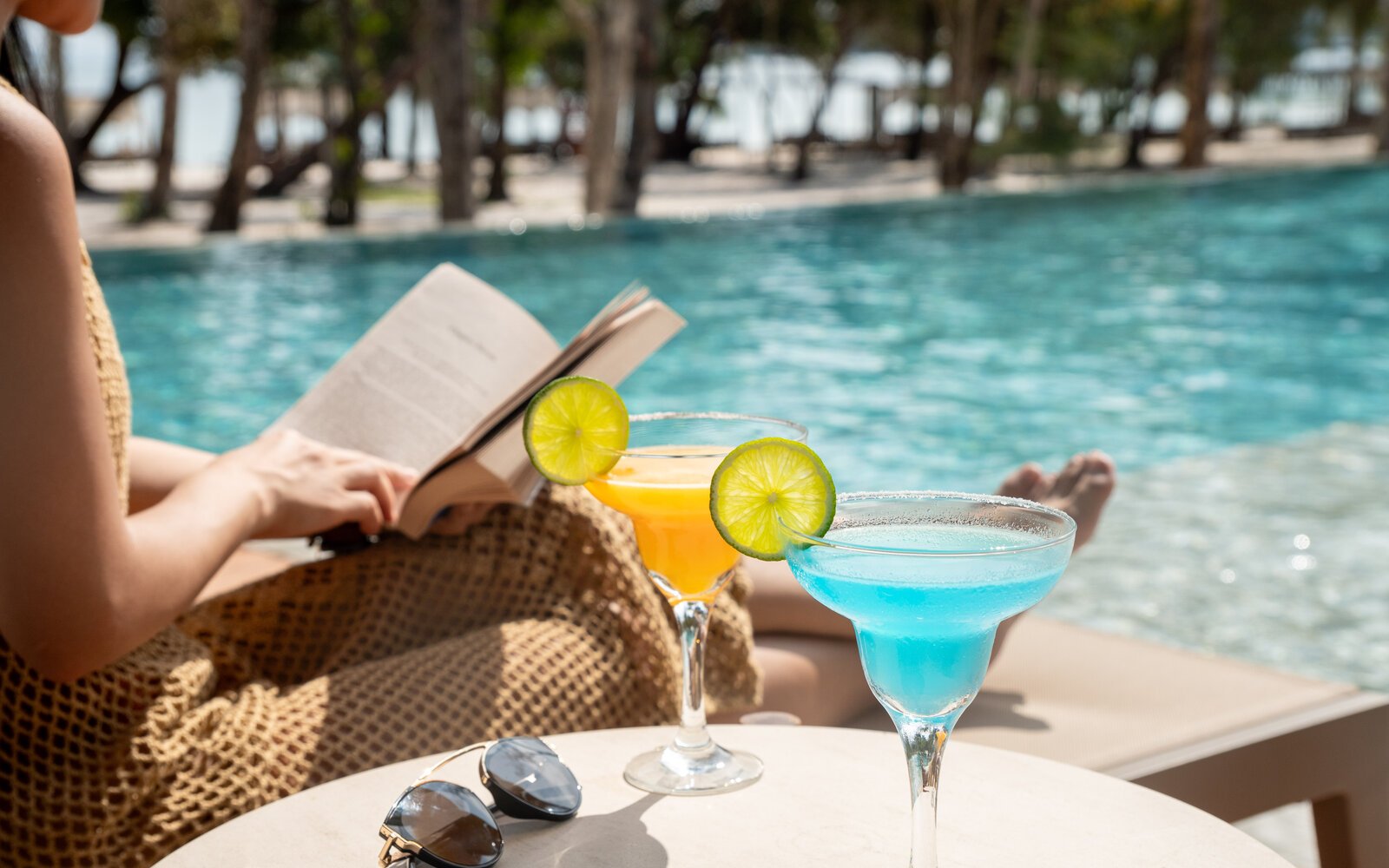 Two colorful tropical cocktails by the pool with a guest reading in the background, at Island Center Point, Koh Rong Sanloem