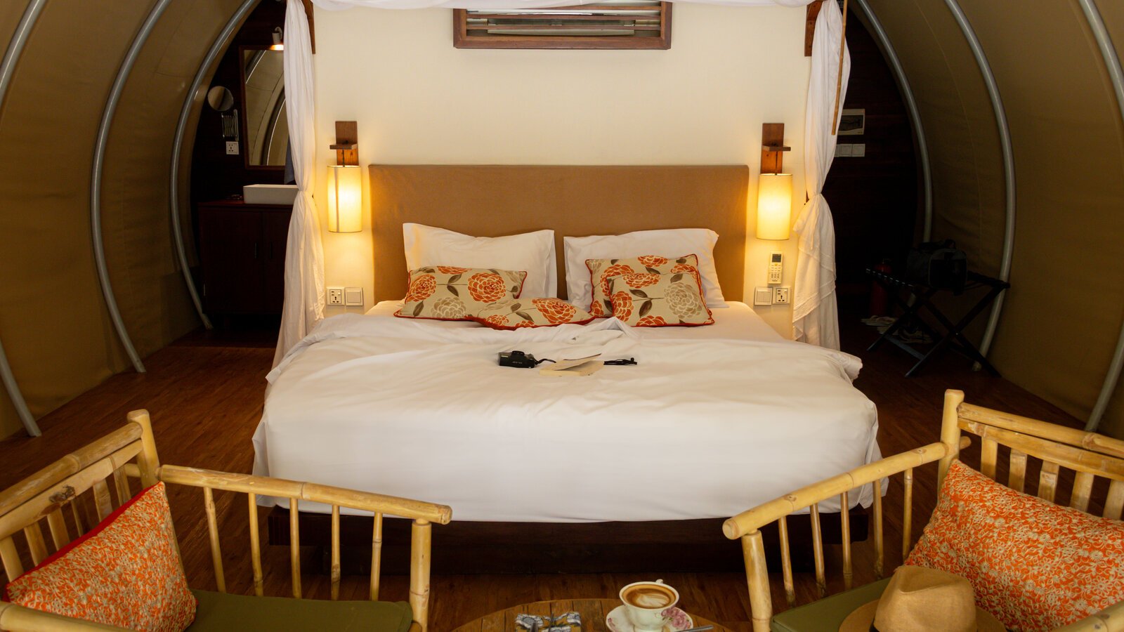 View of a king bed with patterned accent pillows, with two bamboo armchairs positioned in the foreground.