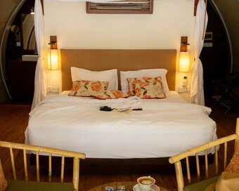 View of a king bed with patterned accent pillows, with two bamboo armchairs positioned in the foreground.