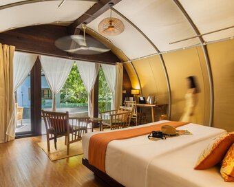 View inside the tented room featuring a bed with orange accents, wooden flooring, a ceiling fan, and large glass doors opening directly out to the pool.