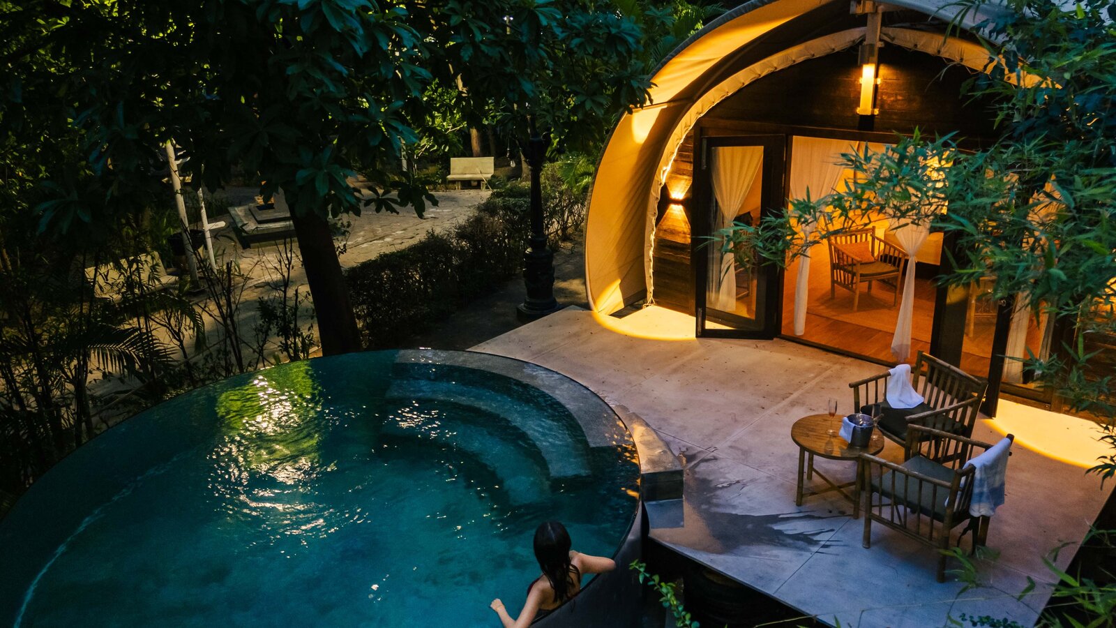 Elevated view at twilight showing the guest lounging on the edge of the private plunge pool, with glowing tented cabin.