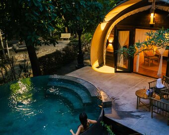 Elevated view at twilight showing the guest lounging on the edge of the private plunge pool, with glowing tented cabin.