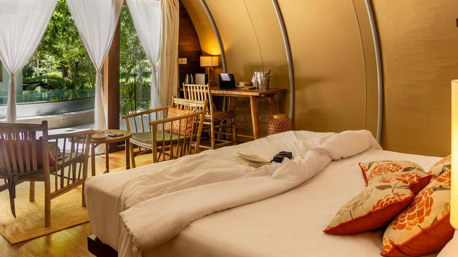 Warm tone bedroom layout with bamboo chairs and open doors leading out to the designer plunge pool.