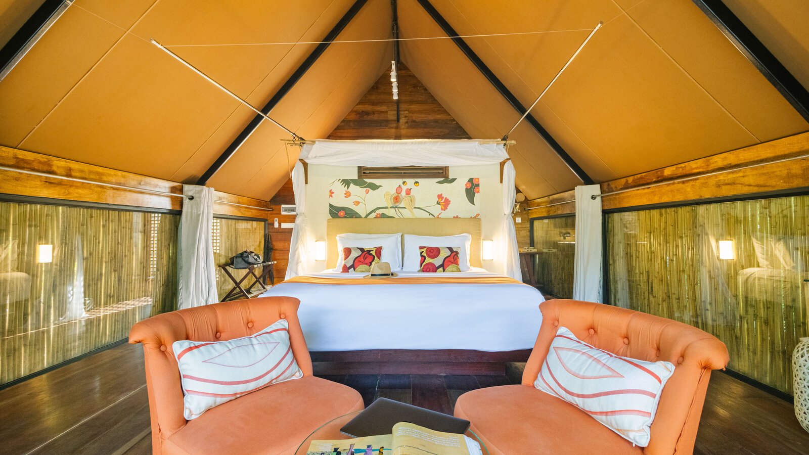 Light-filled and warm interior of a canvas-tented jungle cabin, featuring a king bed with patterned pillows.