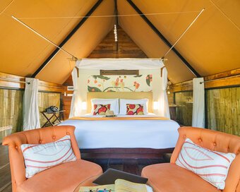 Light-filled and warm interior of a canvas-tented jungle cabin, featuring a king bed with patterned pillows.
