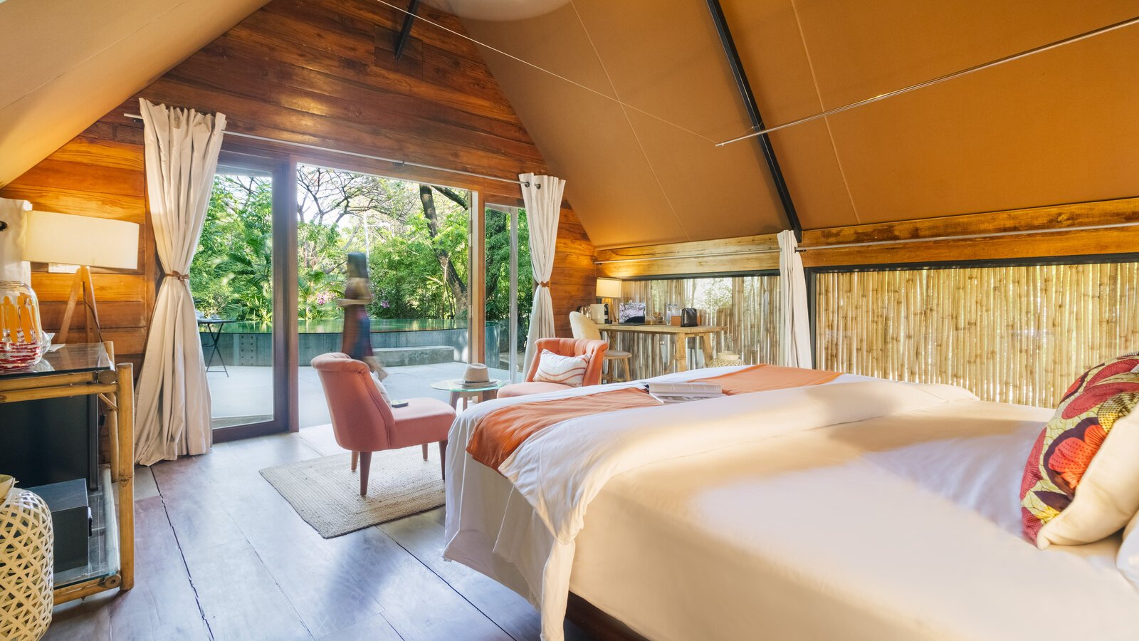Airy bedroom with bamboo wall accents opening directly toward the outdoor pool and garden view.