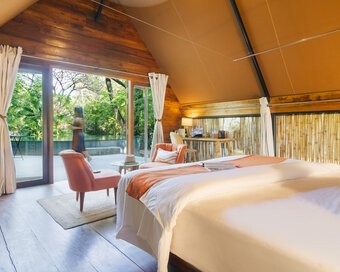 Airy bedroom with bamboo wall accents opening directly toward the outdoor pool and garden view.