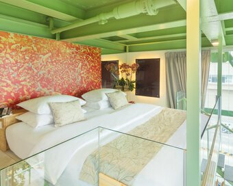 Loft bedroom inside the water tower with a king bed, green steel beams, and a colorful red headboard.