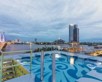 Evening view of the rooftop pool with blue Kbach artwork, looking out over a lit-up bridge and river.