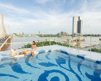 Rooftop swimming pool with a blue artwork patterned floor overlooking the bridge and river during the day.