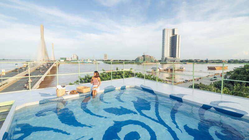 Rooftop swimming pool with a blue artwork patterned floor overlooking the bridge and river during the day.
