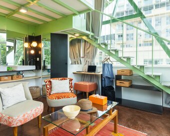Angled view of the water tower living space with chairs, coffee table, bathroom vanity, and green stairs leading up to the loft bed.