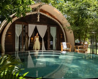 Evening view of a Jungloo unit, reflecting on the surface of its private plunge pool, with a person seated on the deck.