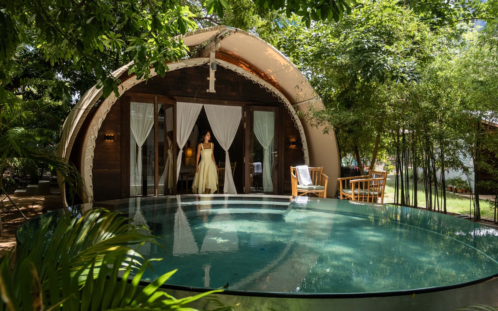 Evening view of a Jungloo unit, reflecting on the surface of its private plunge pool, with a person seated on the deck.