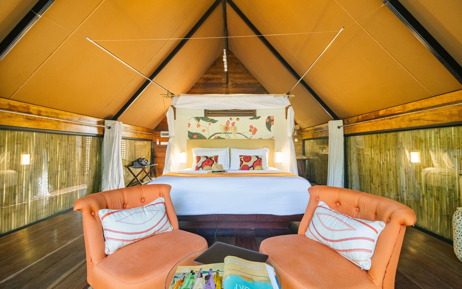 Interior view of Park Jungloo bed area, underneath a high triangular tent ceiling, with two orange sofa chairs and coffee table.