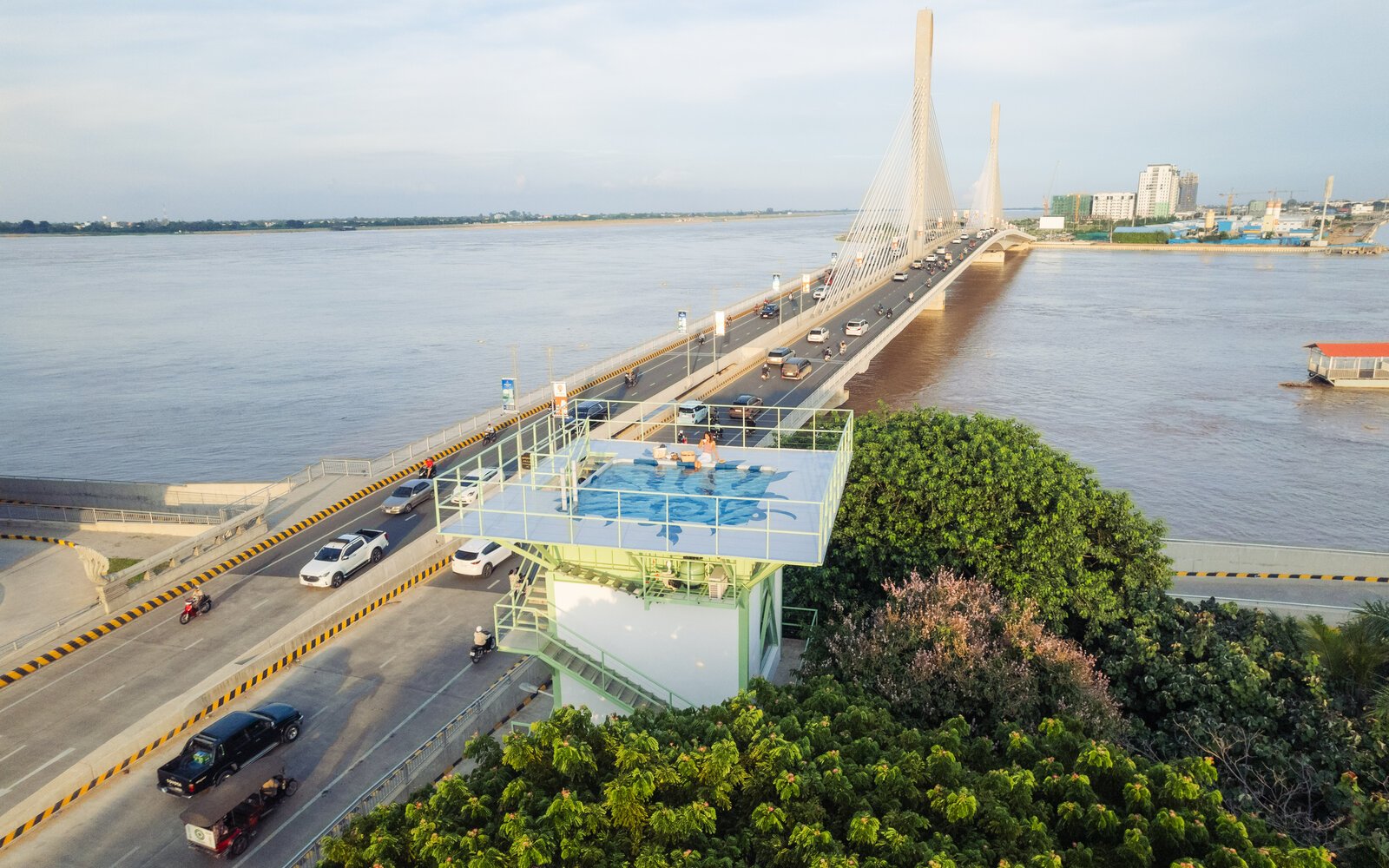 Elevated aerial view of the rooftop pool with people sitting on the deck, with the bridge over a river during the day.