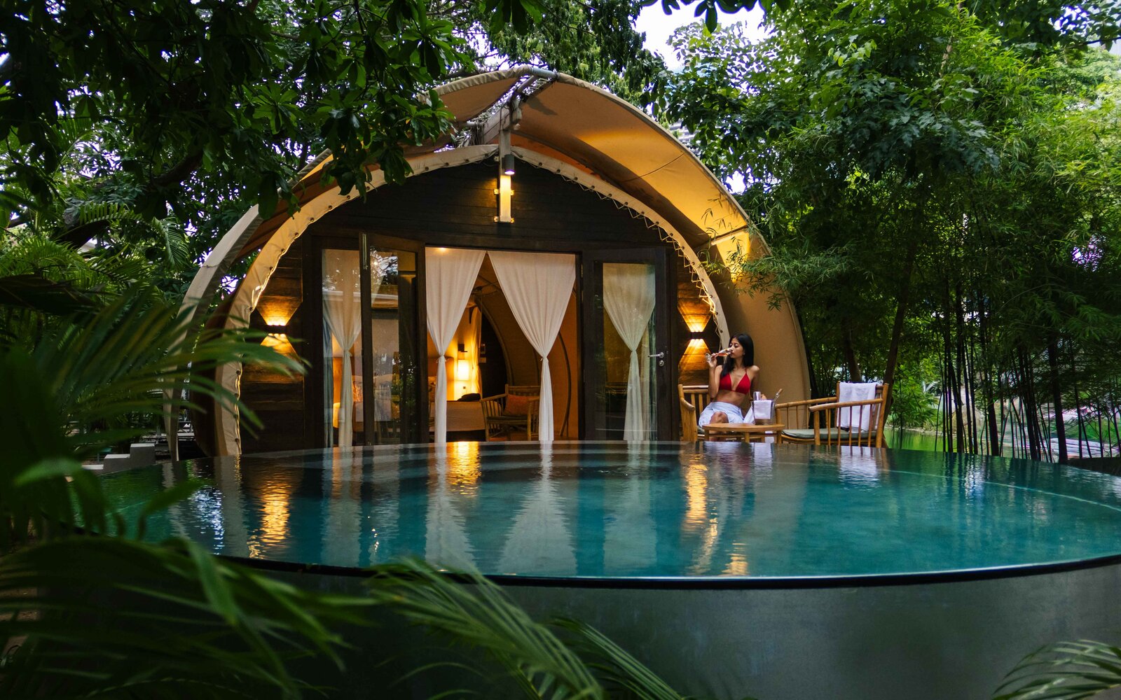 Evening view of Jungloo unit, reflecting on the surface of its private plunge pool, with a person seated on the deck.