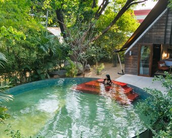 Elevated view of the round swimming pool with red steps, the guest is lounging, with forest trees around.