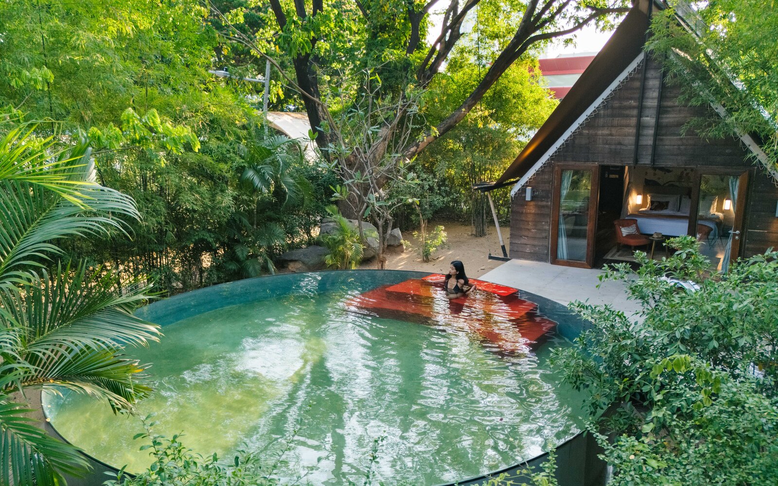 Elevated view of the round swimming pool with red steps, the guest is lounging, with forest trees around.