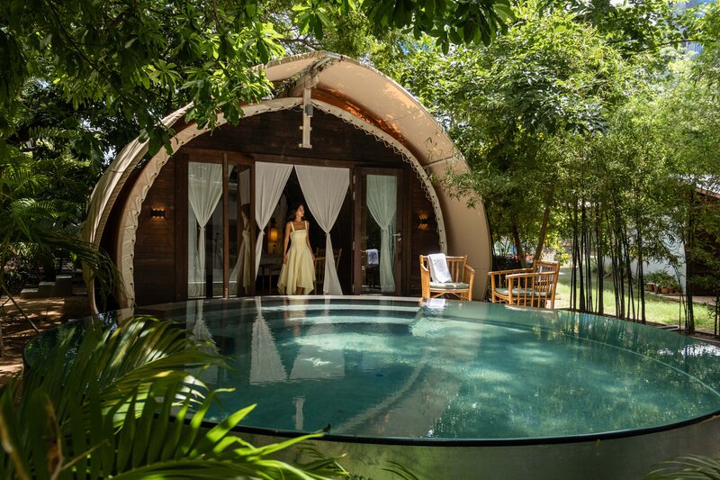 a woman stands at the door of a Jungloo - tented bungalow - in Phnom Penh