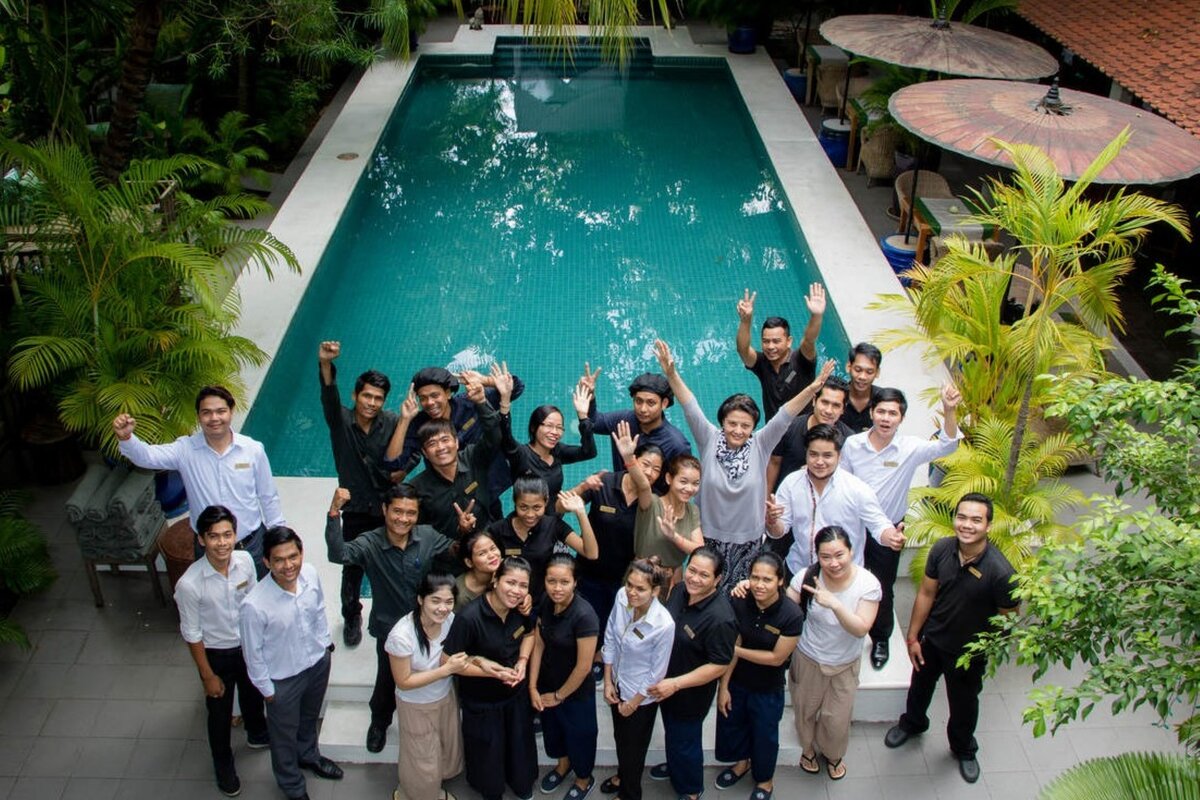 Pavilion team gather around the pool for a team photo, many with arms raised and palm trees on every side.