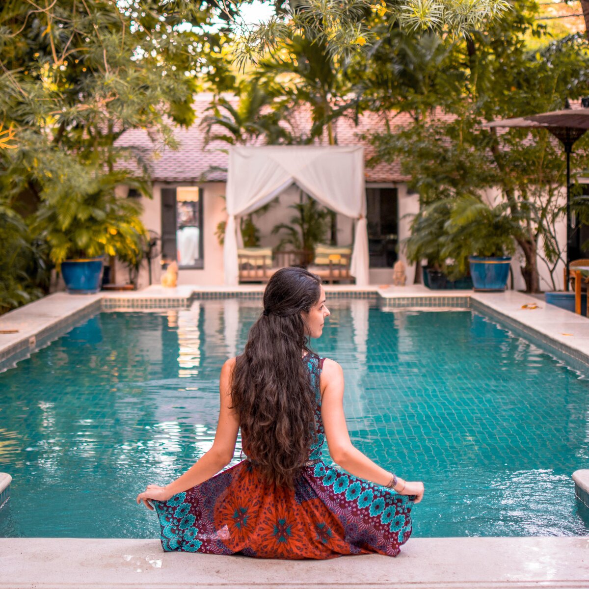 Pavilion guest sits at the poolside with trees and garden view.