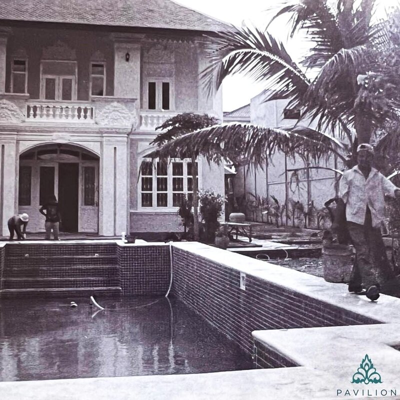 Workers during renovation of the pool in black-and-white photo, with a palm tree and the original building behind them.