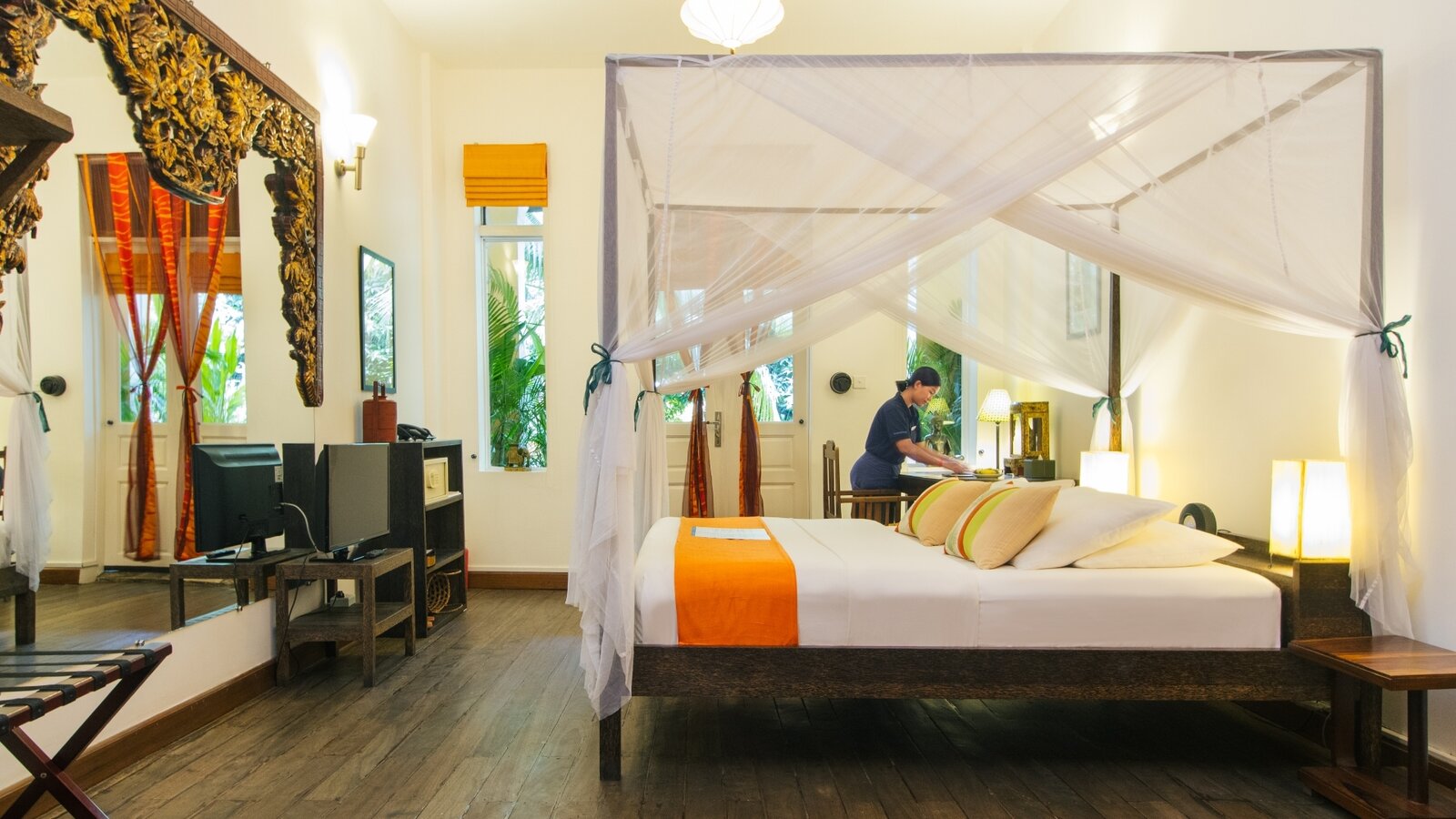 Double Deluxe Room interior with queen bed white large carved mirror in front, and housekeeping staff preparing the room at Pavilion Hotel, Phnom Penh