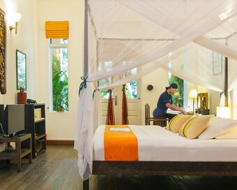 Double Deluxe Room interior with queen bed white large carved mirror in front, and housekeeping staff preparing the room at Pavilion Hotel, Phnom Penh
