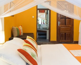 Queen bed with mosquito net, seating area, guest bathrobe, and bathroom entrance in a Double Deluxe Room at Pavilion Phnom Penh