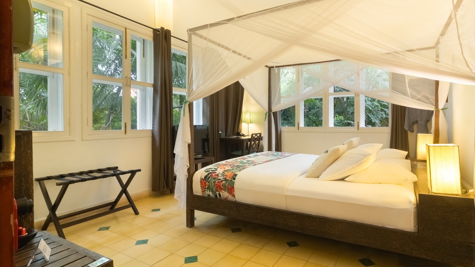 King-size bed with mosquito net, floral bed runner and garden-facing windows in a Pavilion Suite