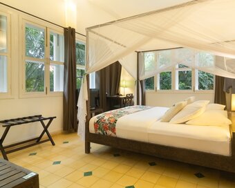 King-size bed with mosquito net, floral bed runner and garden-facing windows in a Pavilion Suite